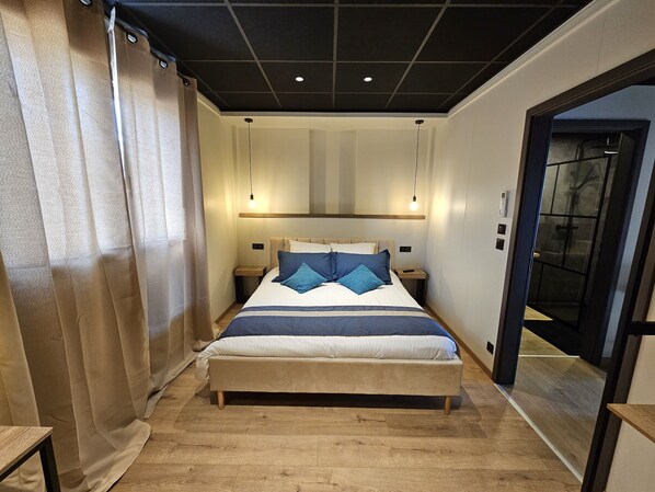 A modern bedroom with a large bed, bedside tables, and a ceiling light fixture. - Gite 4 - 4 Personnes (Dommartin-la-Chaussée)