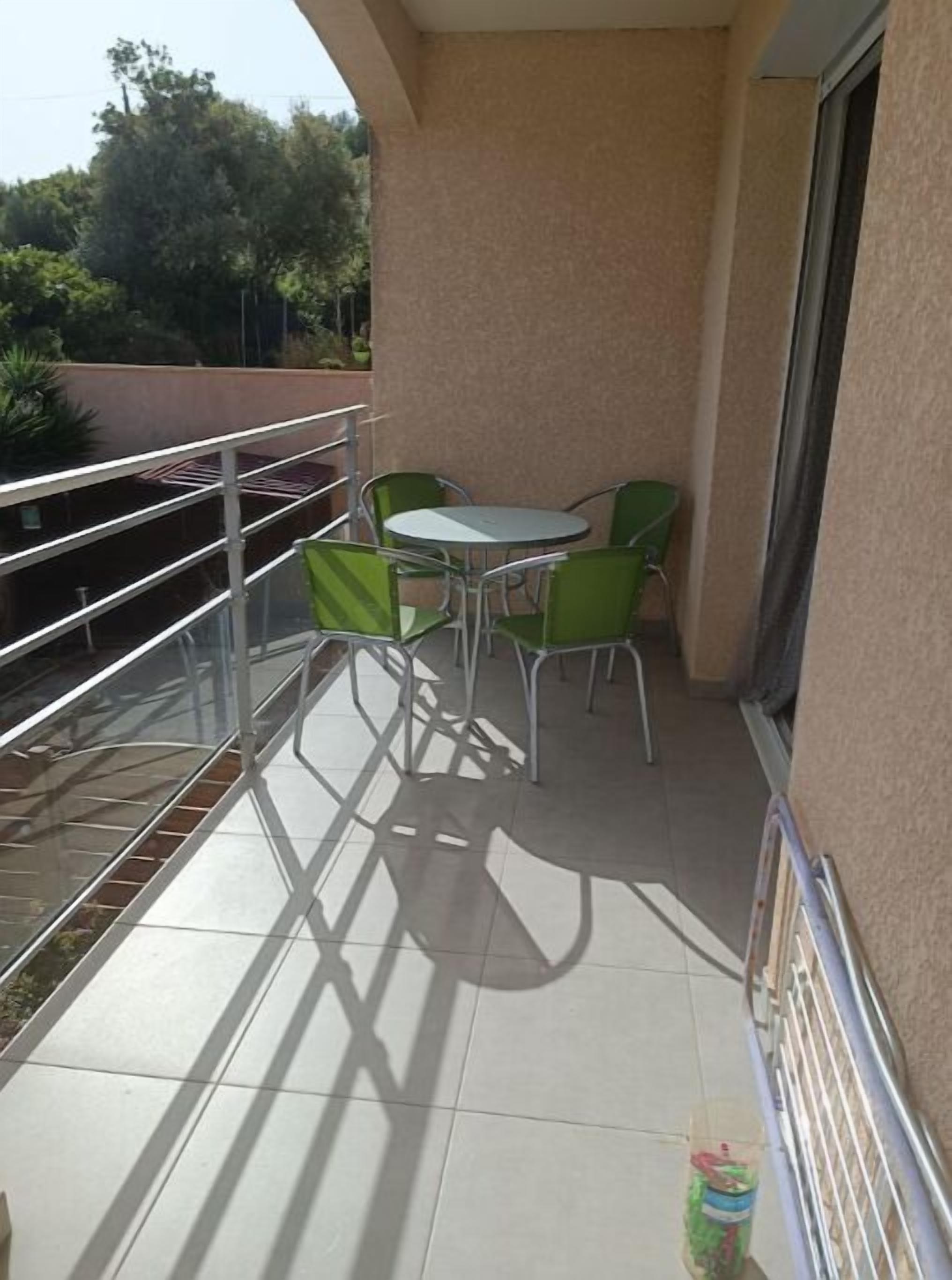 Een balkon met een tafel en stoelen, een metalen hekwerk en uitzicht op bomen en gebouwen.