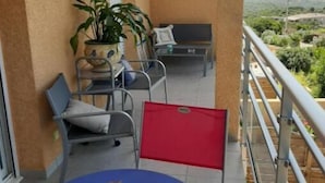 Un balcón con una mesa azul, sillas, un separador plegable rojo y plantas en macetas.