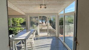 A covered patio with a table and chairs, large sliding glass doors leading to an outdoor area with a view of trees and a fence. - Appartement T3 - 50M de la Plage -rupione (Pietrosella)