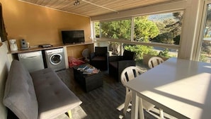 A compact living space with a sofa, a small table, a washing machine, and a TV. - Appartement T3 - 50M de la Plage -rupione (Pietrosella)
