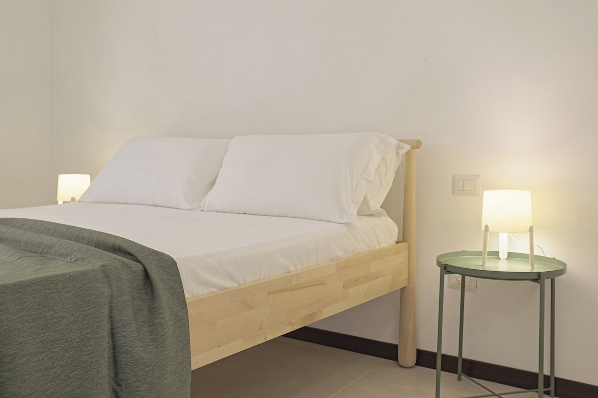 A bed with white linens, a green throw blanket, and two bedside lamps on matching side tables.