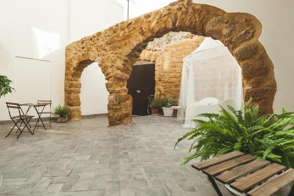 A stone archway leading to a room with a white door, a small table with chairs, and potted plants.