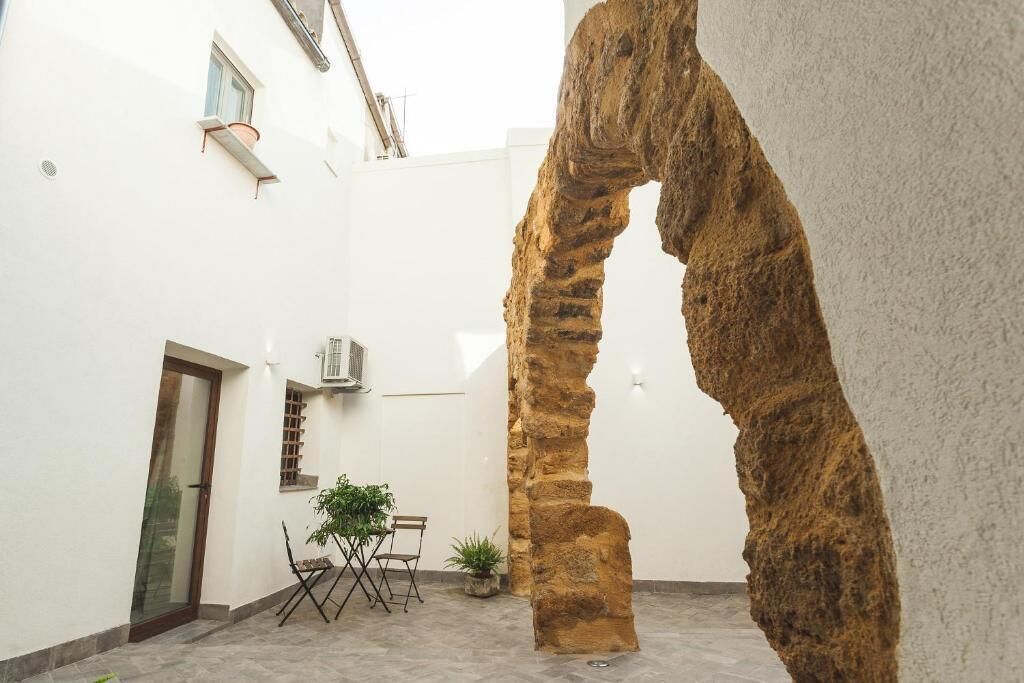 Un cortile con un arco in pietra, una porta, un tavolino con sedie e una pianta in vaso.
