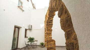 Un cortile con un arco in pietra, una porta, un tavolino con sedie e una pianta in vaso.