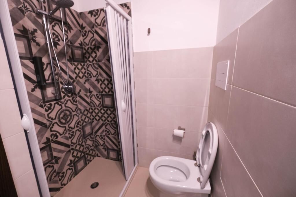 A bathroom with a patterned shower wall, a toilet, and a showerhead.