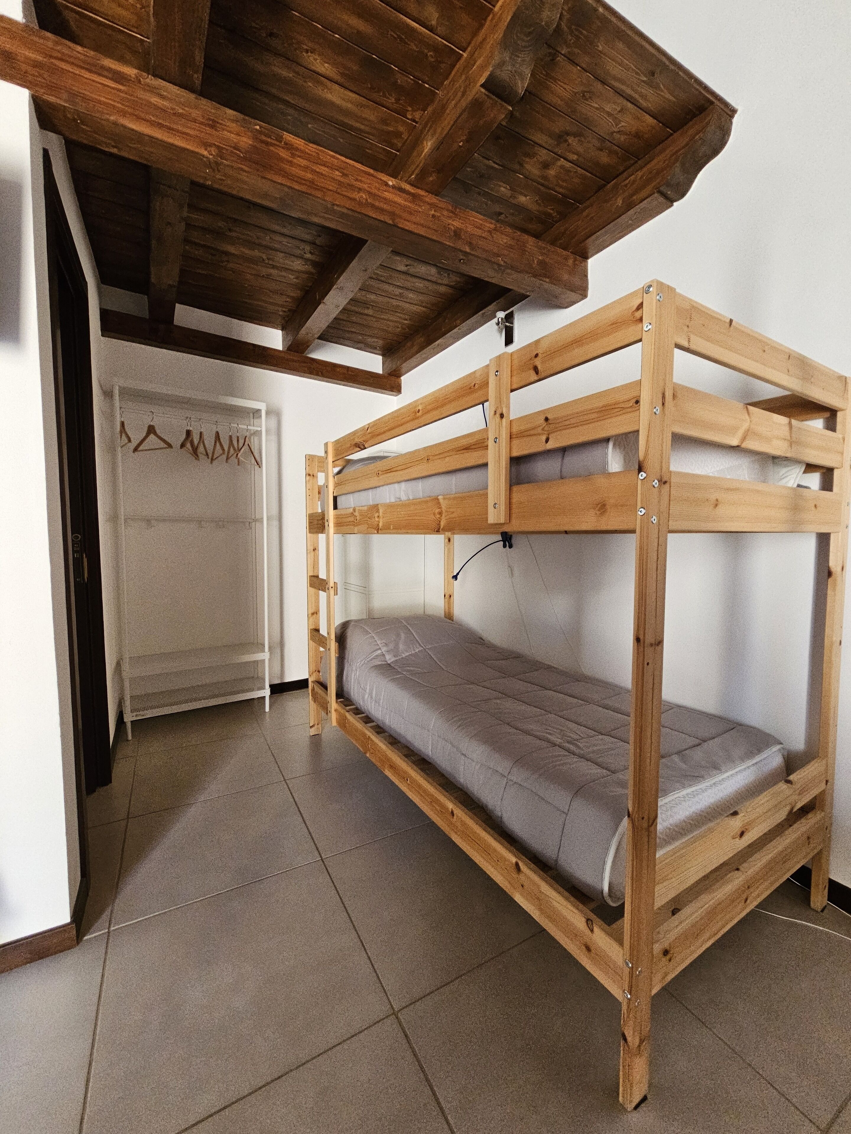 A bunk bed with a wooden frame and a grey mattress in a room with tiled flooring and a white door.