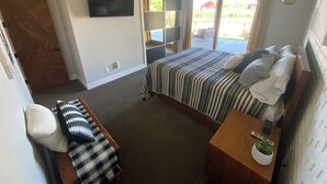 Une chambre à coucher avec un lit, un bureau, une chaise, une télévision et une grande fenêtre.
