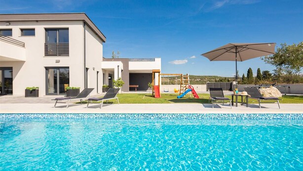 Ein modernes Haus mit Swimmingpool, Rutsche und Liegestühlen.
