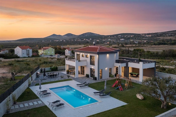 Une maison moderne à deux étages dotée d’une piscine, d’un espace salon extérieur et d’un toboggan.