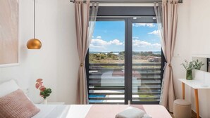 Ein Schlafzimmer mit Bett, Nachttisch, Pendelleuchte, einem Fenster mit Vorhängen und Blick ins Freie.
