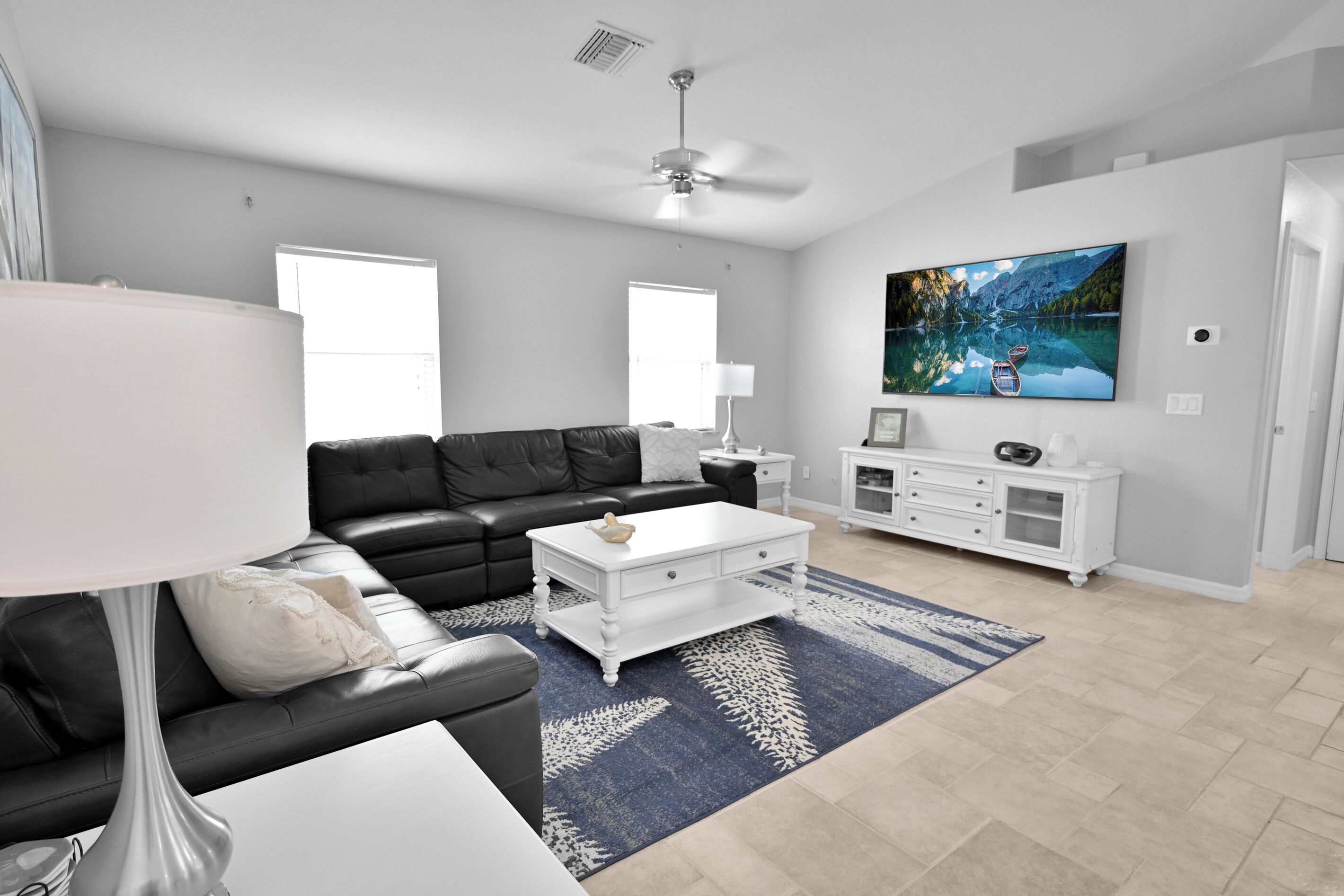 Una sala de estar moderna con un sofá de cuero negro, una mesa de centro blanca y un televisor grande en la pared.
