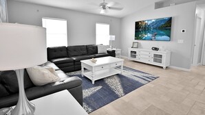 A modern living room with a black leather sofa, white coffee table, and a large TV on the wall. - 4BR | Solar-Powered Heated Pool | Sleeps 8 (Cape Coral)