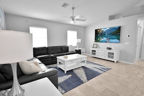A modern living room with a black leather sofa, white coffee table, and a large TV on the wall. - 4BR | Solar-Powered Heated Pool | Sleeps 8 (Cape Coral)