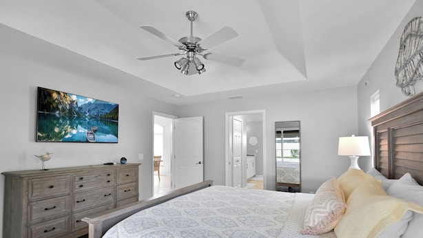 A bedroom with a bed, a ceiling fan, a dresser, a painting, and a lamp. - 4BR | Solar-Powered Heated Pool | Sleeps 8 (Cape Coral)