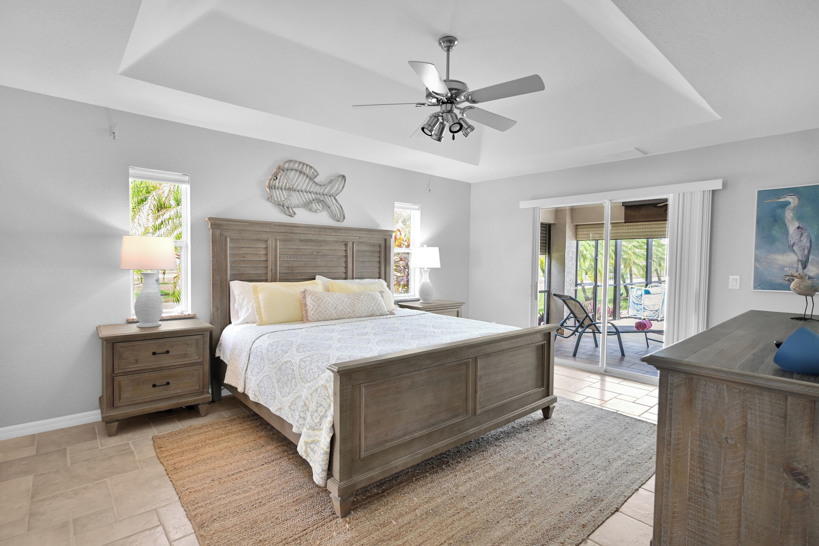 Une chambre à coucher comprenant un lit, des tables de chevet, un ventilateur de plafond, une grande fenêtre et une vue sur l’extérieur.