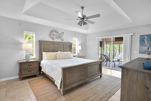 A bedroom with a bed, nightstands, a ceiling fan, a large window, and a view of the outdoors. - 4BR Cape | Solar Pool | Bikes Included (Cape Coral)