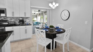 A modern kitchen with white cabinets, a black countertop, and a dining area with a round table and white chairs. - 4BR | Solar-Powered Heated Pool | Sleeps 8 (Cape Coral)