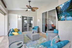 A sunlit patio with wicker furniture, a ceiling fan, and a large sliding glass door leading to an interior space. - 4BR Cape | Solar Pool | Bikes Included (Cape Coral)