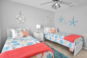 Une chambre avec deux lits, un ventilateur de plafond et des œuvres d’art décoratives au mur.