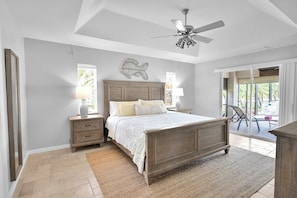 Une chambre avec un lit en bois, des tables de chevet, un ventilateur de plafond et une vue sur l’extérieur.