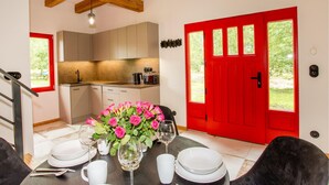 A dining area with a table set for four, a red door, and a kitchen in the background. - Beach front home in Rowy with WiFi (Rowy)