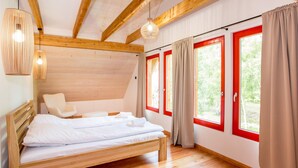 A bedroom with a wooden bed, a chair, a hanging light fixture, and large windows with red frames. - Beach front home in Rowy with WiFi (Rowy)
