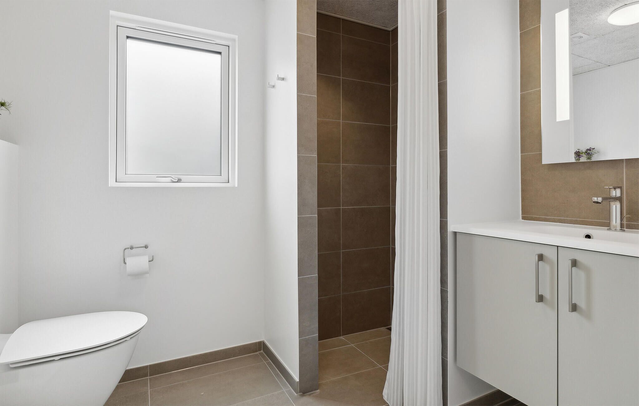 Een badkamer met toilet, douche met gordijn en wastafel met spiegel.