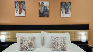 Une chambre d’hôtel comprenant un lit, deux tables de chevet, un climatiseur fixé au mur et trois œuvres d’art murales représentant des motifs de feuilles.