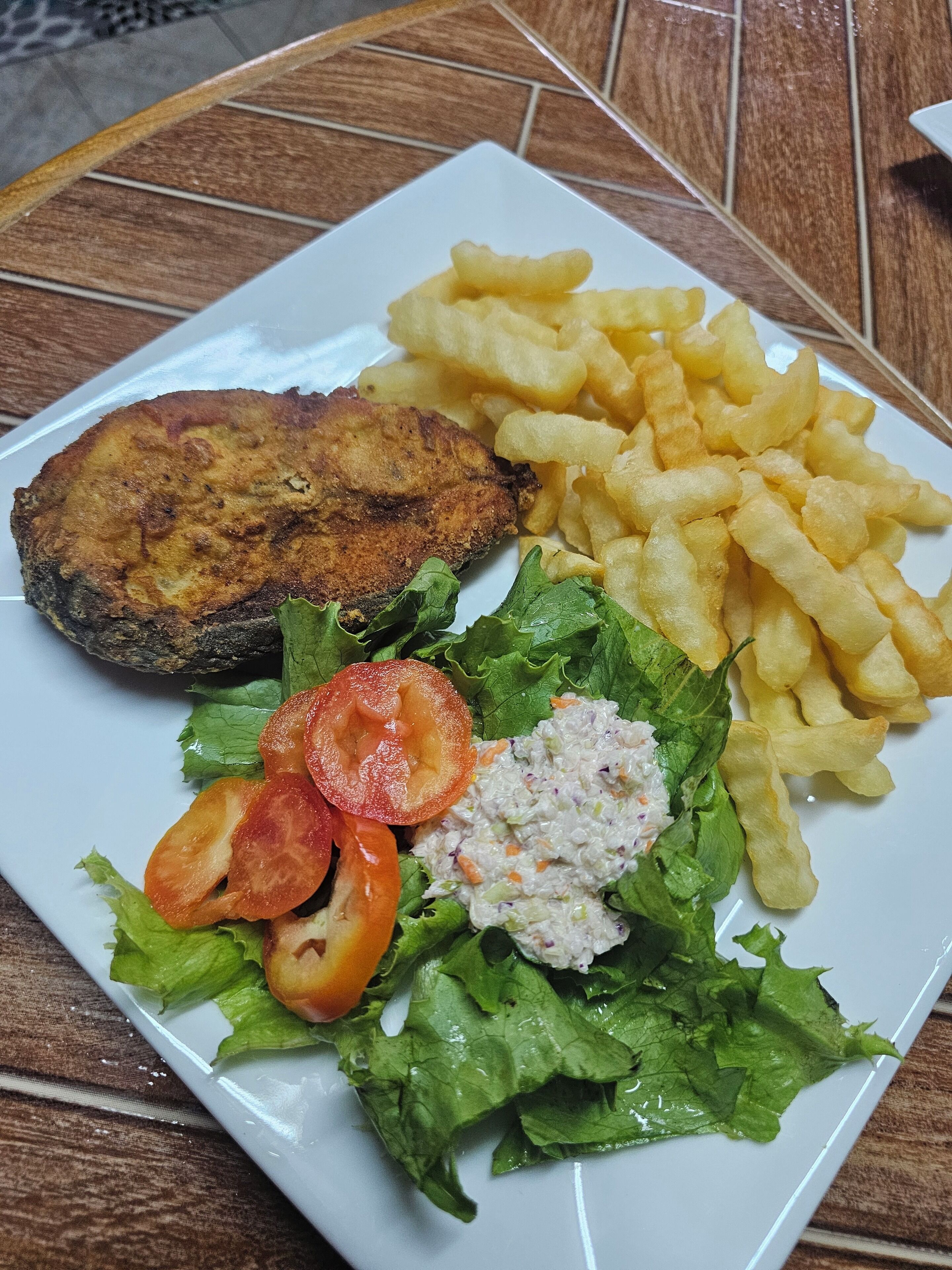 A plate with a fried fish, French fries, lettuce, and a side salad.