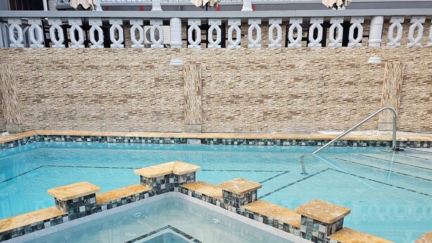 Une piscine bordée de pierres, avec une terrasse en pierre aménagée avec des sièges.