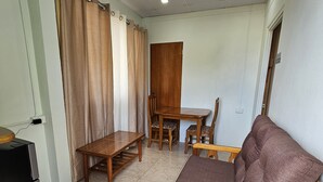 Un salon avec un canapé en bois, une table à manger en bois avec des chaises, un meuble noir et un plafond doté d’un éclairage encastré.