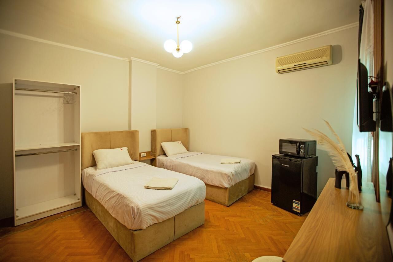 A room with two beds, a wardrobe, a desk with a computer, and an air conditioning unit.