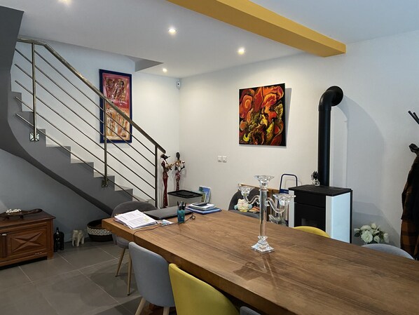 Un salon moderne avec une table à manger en bois, un escalier et deux tableaux abstraits accrochés aux murs.