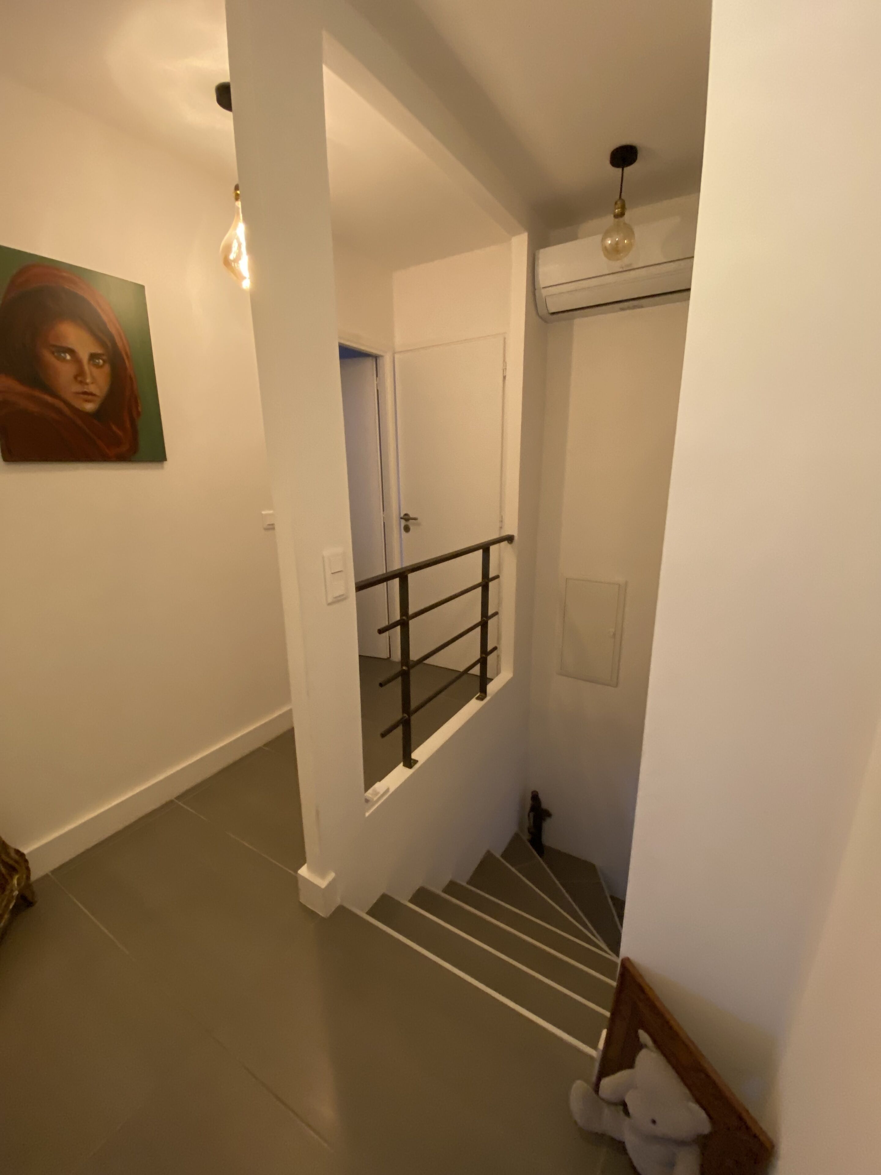 Uma escada com corrimão, uma porta que dá para outro cômodo e um ponto de luz fixado na parede.