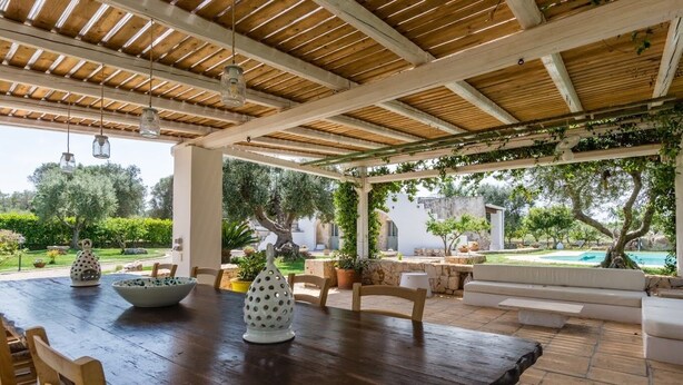 Un espacio para comer al aire libre con techo, una mesa de madera, sillas y elementos decorativos.