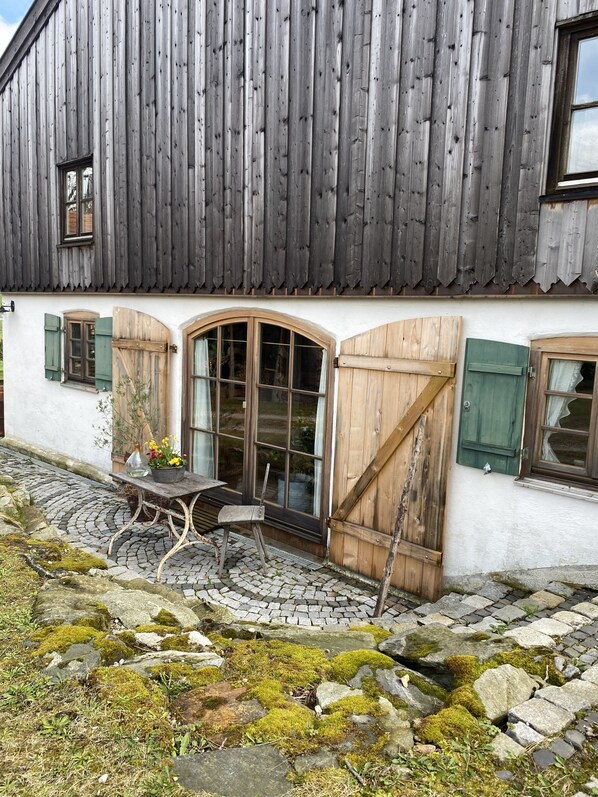 Un edificio rústico con fachada de madera, un patio empedrado de piedra y una mesa con sillas afuera.