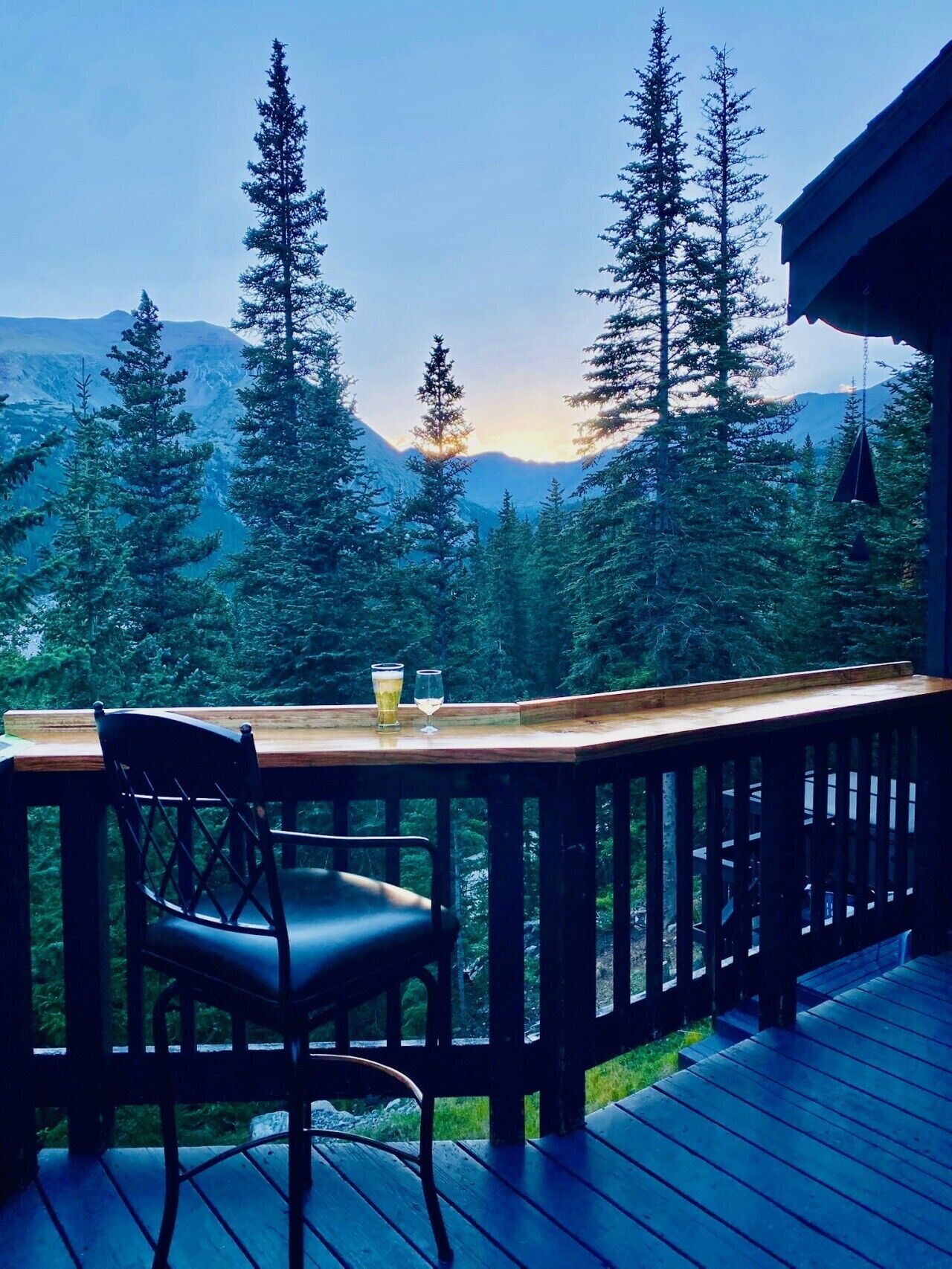 Une terrasse en bois avec une table et des chaises, offrant une vue sur une chaîne de montagnes boisée.