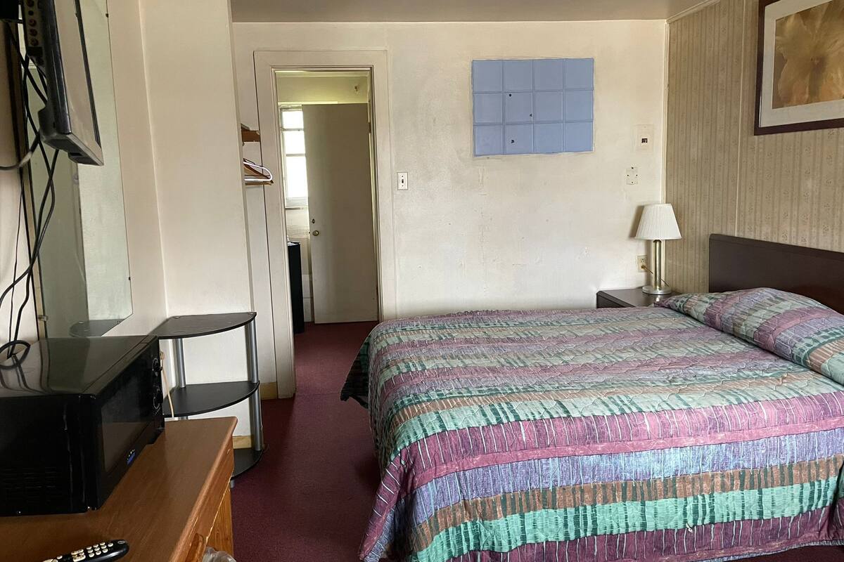 A hotel room with a bed, a desk, a TV, and a door leading to another room.