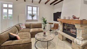 Een woonkamer met een hoekbank, een ronde salontafel, een open haard en een aan de muur bevestigde televisie.