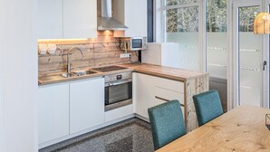 A modern kitchen with white cabinetry, a wooden countertop, a built-in oven, and a microwave. There is a window providing natural light and a view of trees. - 3 bedroom gorgeous apartment in Bad Heilbrunn (Bad Heilbrunn)