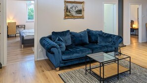 A modern living room with a blue velvet sofa, a glass coffee table, and a framed landscape painting on the wall. - 3 bedroom gorgeous apartment in Bad Heilbrunn (Bad Heilbrunn)