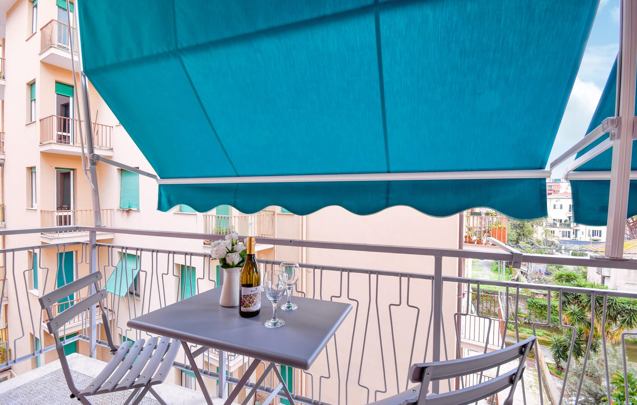 A balcony with a table, chairs, a bottle of wine, and glasses.