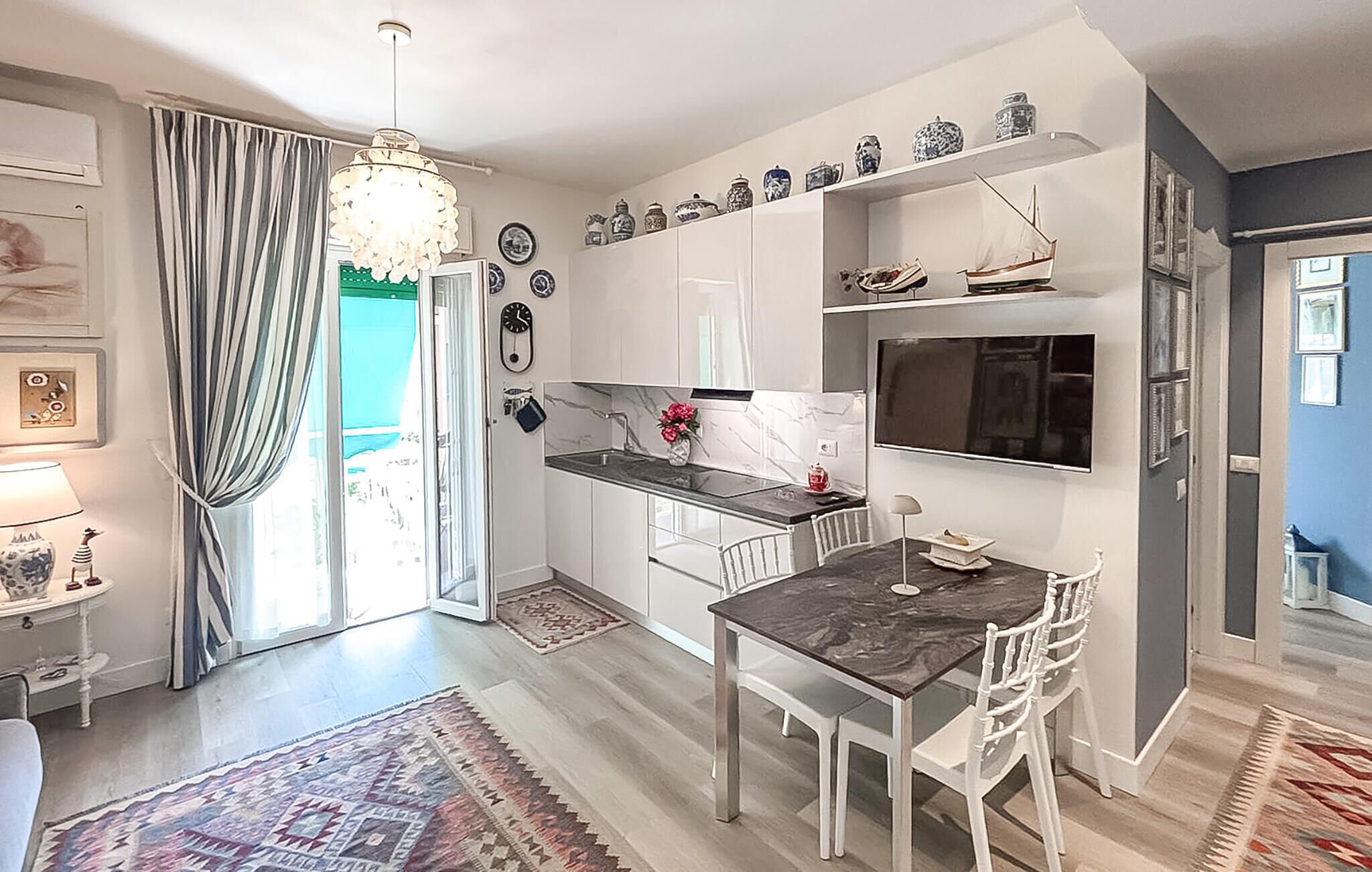 Une cuisine moderne avec des meubles blancs, un plan de travail en marbre et un coin repas comprenant une table foncée et des chaises blanches.