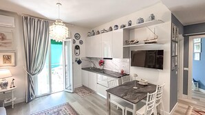 Une cuisine moderne avec des meubles blancs, un plan de travail en marbre et un coin repas comprenant une table foncée et des chaises blanches.