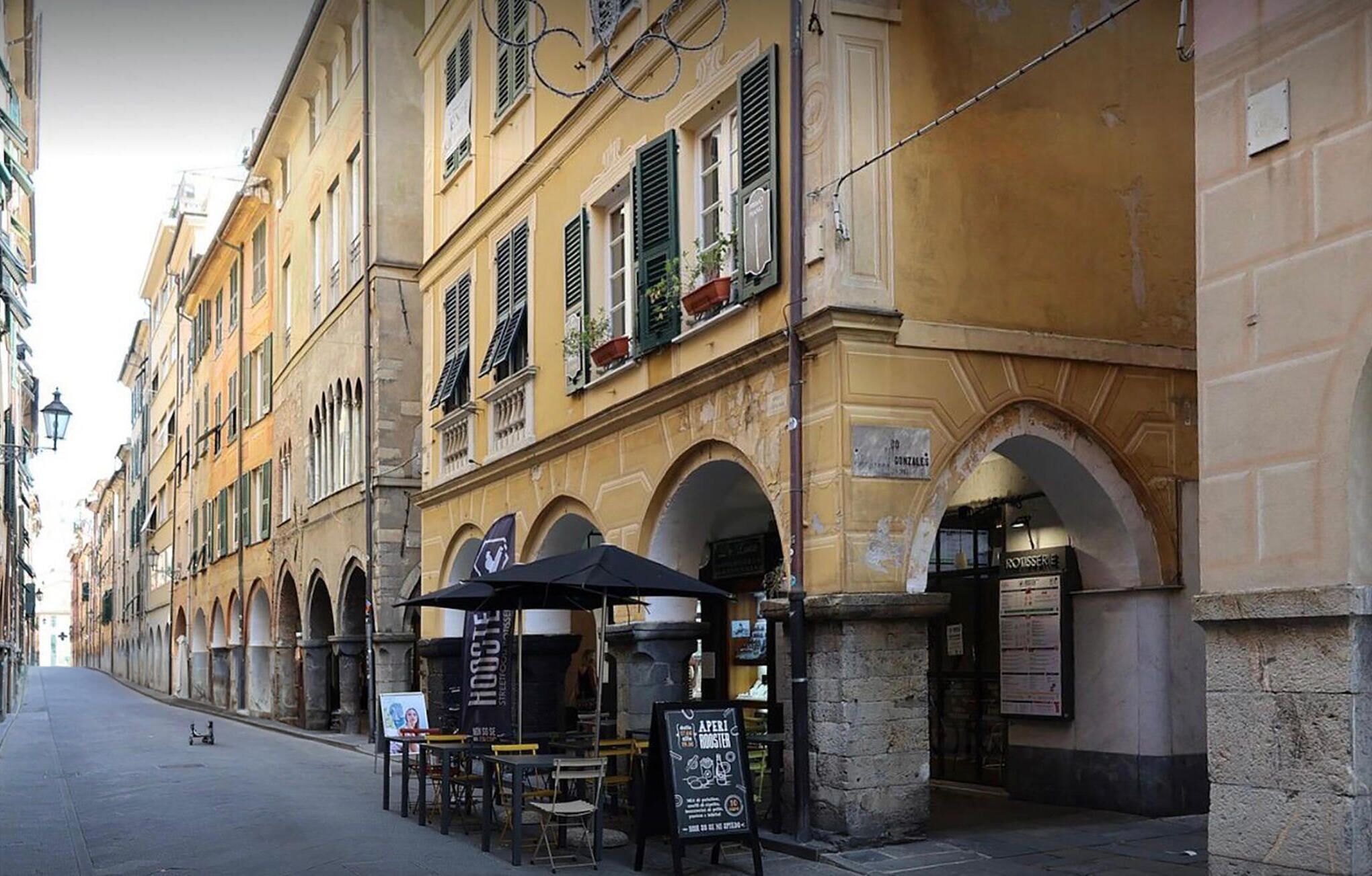 Une rue bordée d’un café situé sous une arche, avec des tables en terrasse, et un immeuble doté de nombreuses fenêtres et de balcons.