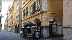 Une rue bordée d’un café situé sous une arche, avec des tables en terrasse, et un immeuble doté de nombreuses fenêtres et de balcons.