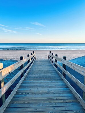 A wooden pier leading to a beach with a clear blue sky.