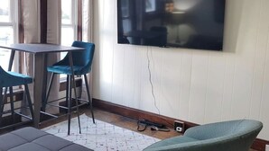 A room with a TV mounted on the wall, a table with chairs, and a sofa.