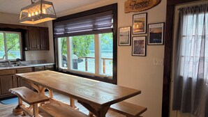 Une cuisine avec une grande table et des bancs en bois, un luminaire suspendu et une fenêtre donnant sur des arbres et une étendue d’eau.